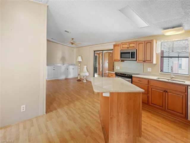 Kitchen with light wood finished floors, appliances with stainless steel finishes, a textured ceiling, a center island, and ceiling fan