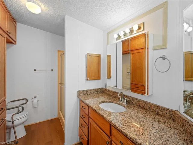 Bathroom with wood finished floors, vanity, a stall shower, and a textured ceiling