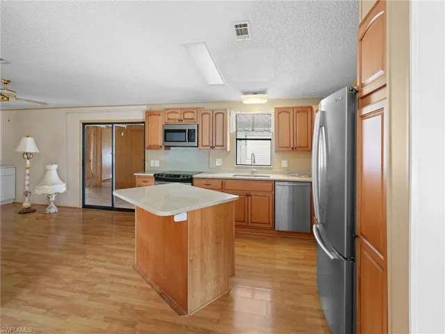 Kitchen featuring light countertops, stainless steel appliances, a kitchen island, a textured ceiling, and light wood finished floors