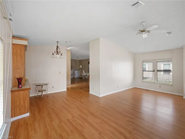 Empty room featuring light wood-style floors, a chandelier, ceiling fan, and a textured ceiling