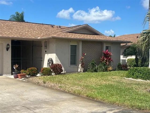 Property entrance featuring roof with shingles, a yard, brick siding, stucco siding, and an attached garage