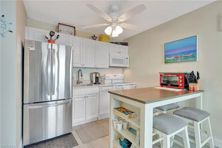 Kitchen featuring white appliances, butcher block counters, a breakfast bar area, white cabinetry, and a textured ceiling