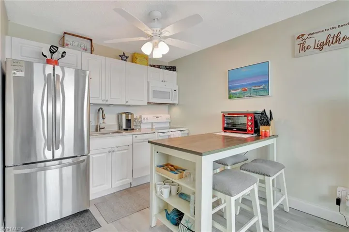 Kitchen featuring white appliances, butcher block countertops, a breakfast bar area, white cabinets, and light wood finished floors