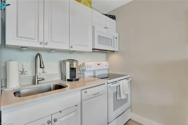 Kitchen featuring white appliances, white cabinets, light stone counters, and a textured ceiling