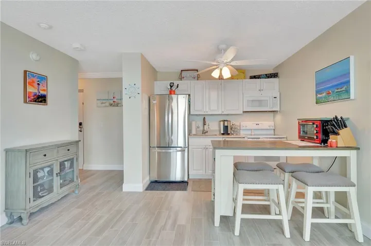 Kitchen featuring white appliances, a kitchen breakfast bar, light countertops, a peninsula, and white cabinetry