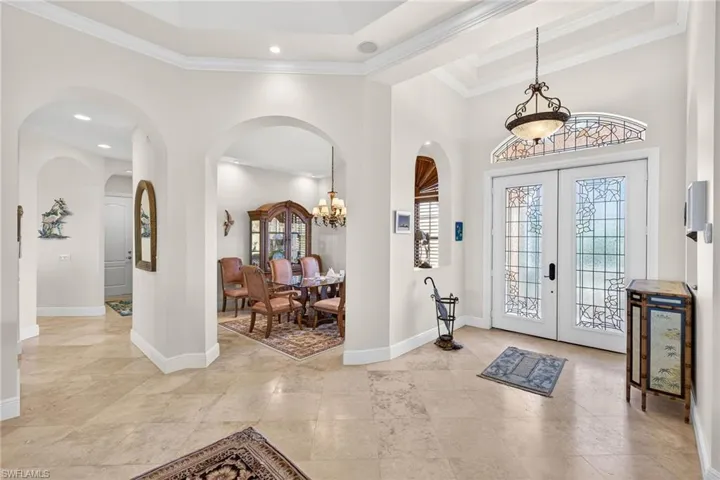 Foyer featuring french doors, crown molding, arched walkways, and a chandelier