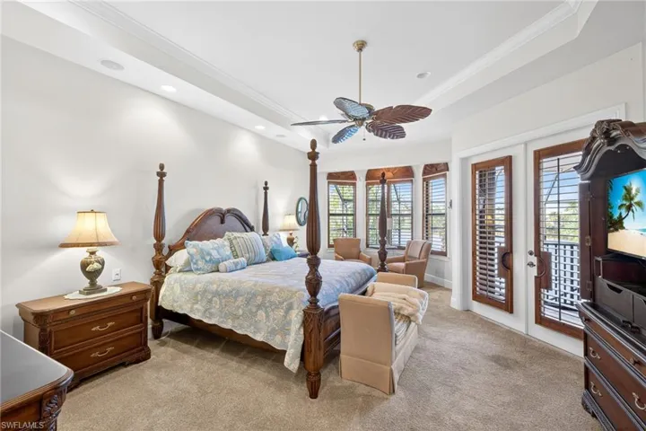 Primary bedroom featuring crown molding, light carpet, access to outside, a tray ceiling, and a ceiling fan