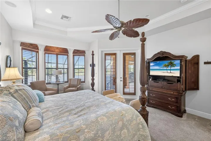 Primary bedroom featuring crown molding, a raised ceiling, access to exterior, ceiling fan, and french doors