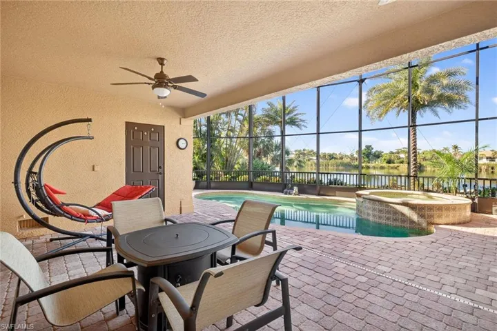 View of patio / terrace featuring glass enclosure, a ceiling fan, a pool with connected hot tub, and outdoor dining space