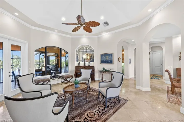 Living room featuring arched walkways, a towering ceiling, crown molding, ceiling fan, and french doors
