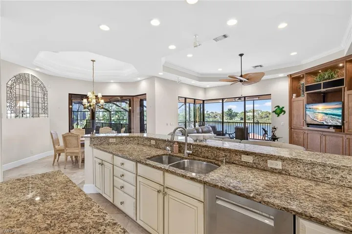 Kitchen with cream cabinets, light stone countertops, dishwasher, decorative light fixtures, and a tray ceiling