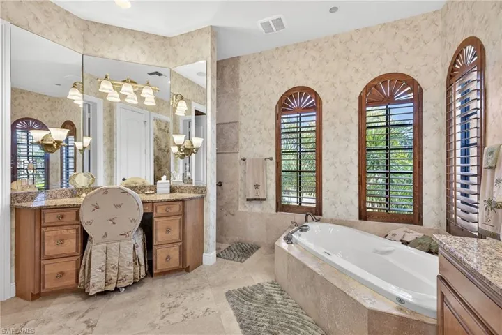 Primary bathroom with a garden tub, vanity, wallpapered walls, and a walk in shower