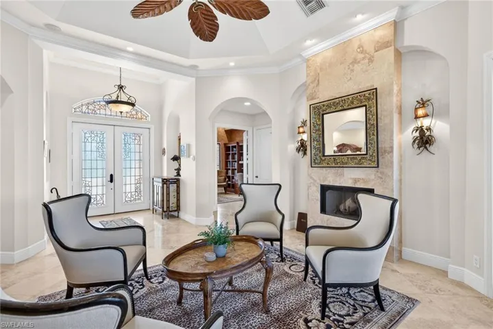 Living room featuring arched walkways, french doors, ornamental molding, a premium fireplace, and a high ceiling