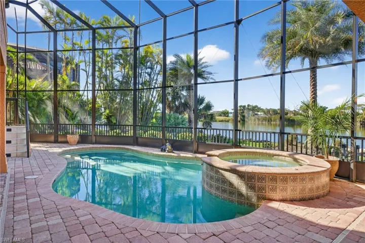 View of swimming pool featuring glass enclosure, a sunroom, a pool with connected hot tub, a water view, and a patio area
