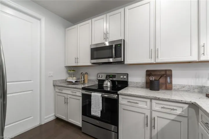 Kitchen with stainless steel appliances, white cabinetry, dark wood-style flooring, and light stone countertops
