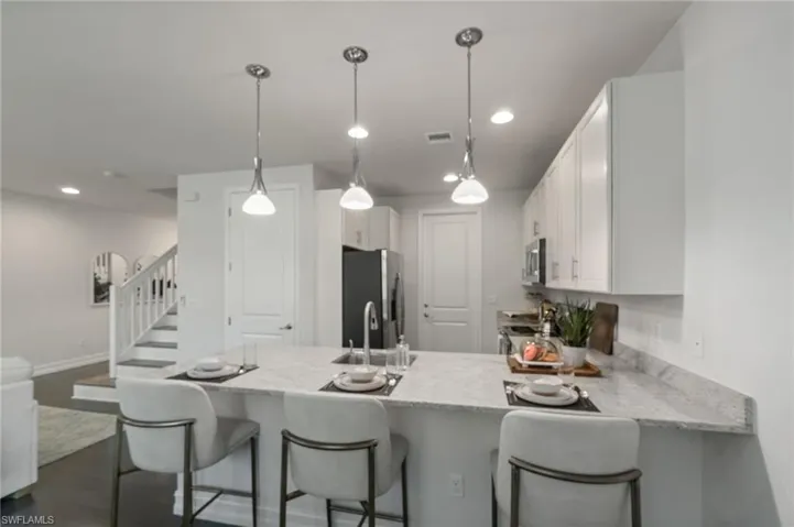 Kitchen featuring a peninsula, a breakfast bar, white cabinets, stainless steel appliances, and pendant lighting