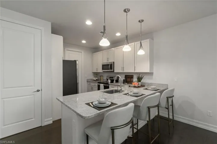 Kitchen featuring a breakfast bar area, a peninsula, stainless steel appliances, white cabinetry, and light granite counters