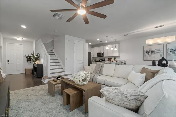 Living area with contrasting large ceiling fan, rich wood-type flooring, bright and recessed lighting is inviting and open.