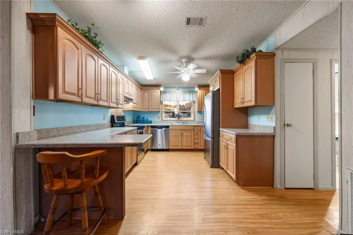 Kitchen featuring appliances with stainless steel finishes, a textured ceiling, light wood finished floors, a kitchen bar, and a ceiling fan
