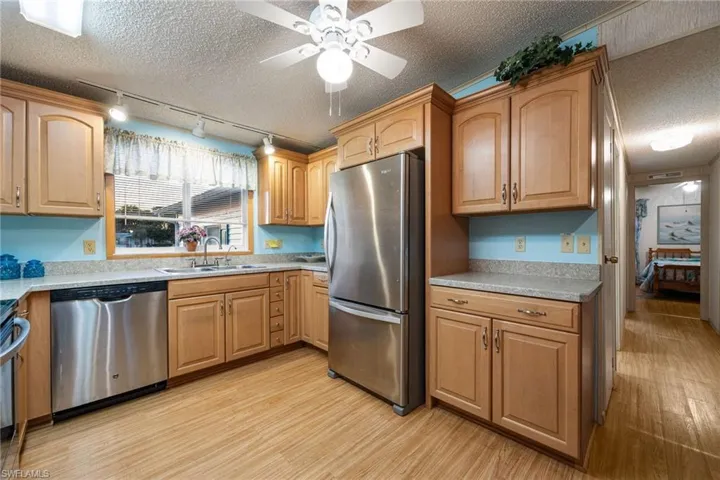 Kitchen with track lighting, a textured ceiling, appliances with stainless steel finishes, light wood-style flooring, and a ceiling fan