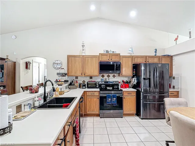 Kitchen featuring black fridge, electric range, backsplash, sink, and light tile floors