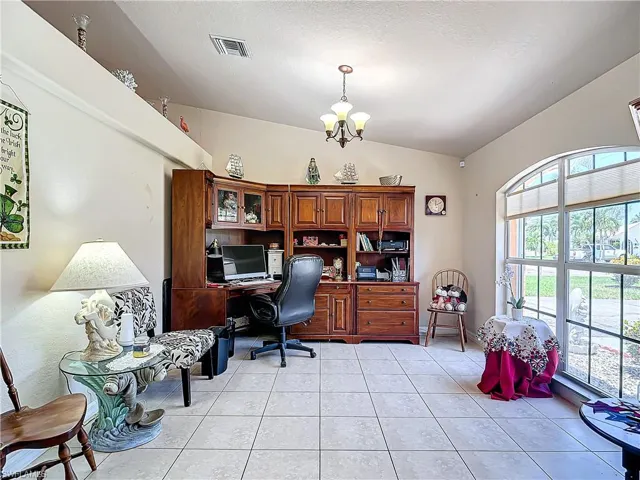 Home office featuring an inviting chandelier, lofted ceiling, and light tile floors