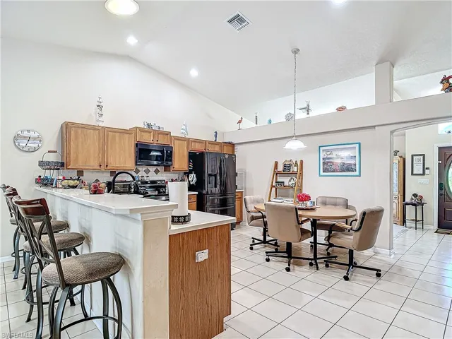 Kitchen with tasteful backsplash, black appliances, high vaulted ceiling, light tile floors, and pendant lighting