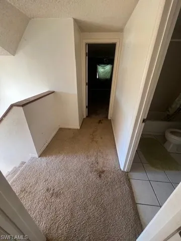 Corridor featuring a textured ceiling and light carpet