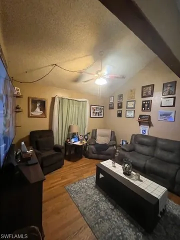 Living room with hardwood / wood-style floors, a textured ceiling, ceiling fan, and lofted ceiling