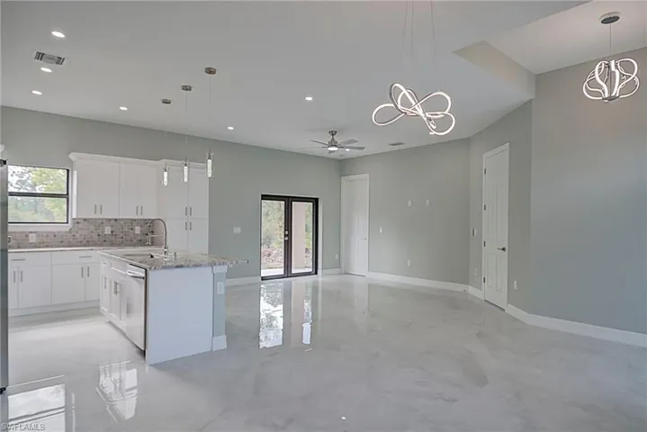 Kitchen featuring pendant lighting, ceiling fan, an island with sink, white cabinets, and backsplash