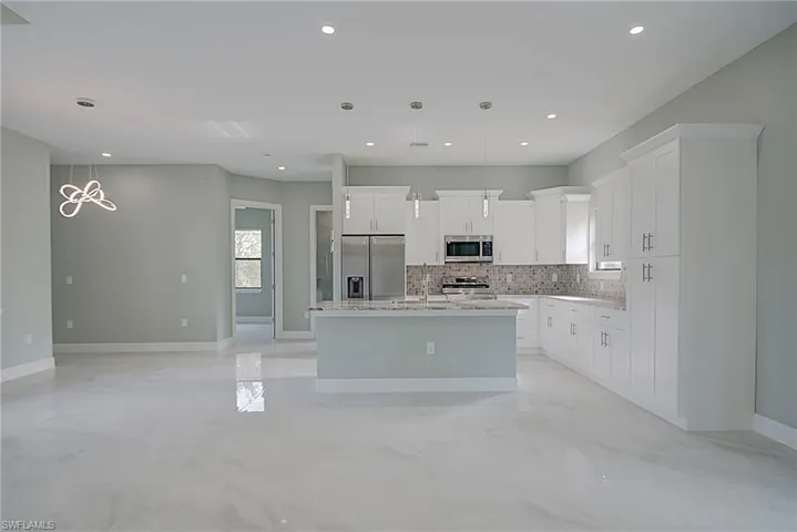 Kitchen with pendant lighting, stainless steel appliances, white cabinets, a kitchen island with sink, and open floor plan