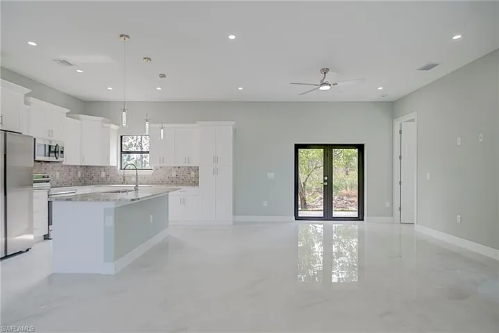 Kitchen with a center island with sink, appliances with stainless steel finishes, white cabinets, pendant lighting, and light stone counters