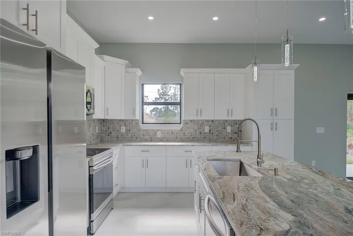 Kitchen featuring appliances with stainless steel finishes, light stone countertops, white cabinets, hanging light fixtures, and recessed lighting