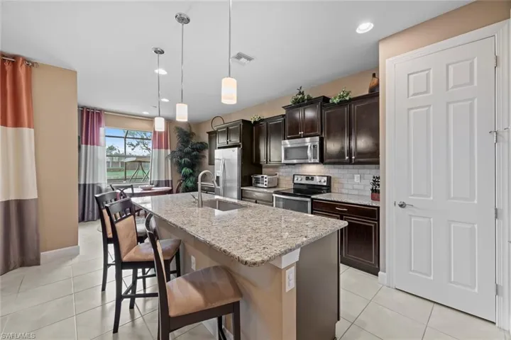 Kitchen with granite counters, tile backsplash and pantry door to the right.  Breakfast nook in the background with view of pond.