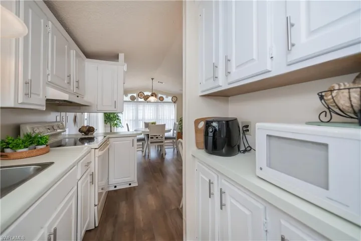 Kitchen featuring white appliances, light countertops, white cabinetry, dark wood-type flooring, and vaulted ceiling