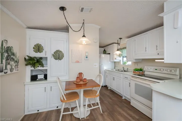 Kitchen featuring white appliances, a textured ceiling, white cabinetry, light countertops, and hanging light fixtures