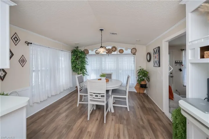 Dining space with lofted ceiling, a textured ceiling, crown molding, and dark wood-style flooring