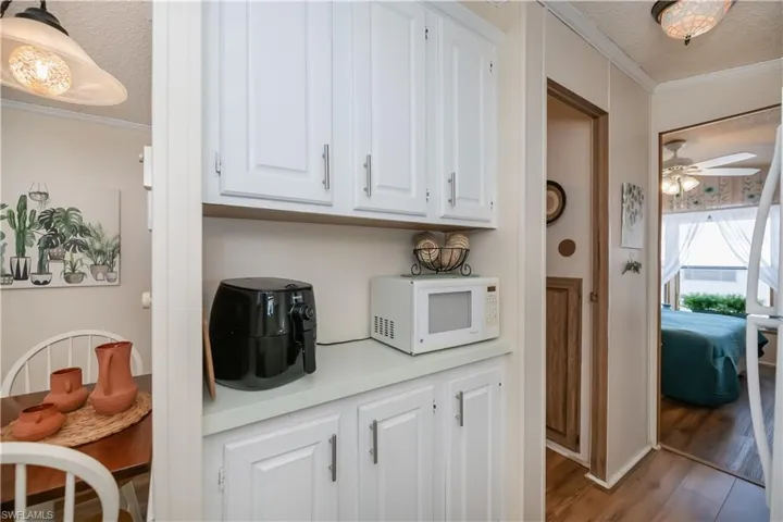Kitchen with crown molding, white cabinetry, white appliances, light countertops, and a textured ceiling