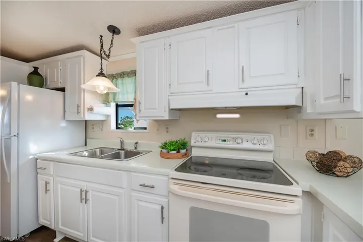 Kitchen featuring white appliances, light countertops, white cabinetry, and decorative light fixtures