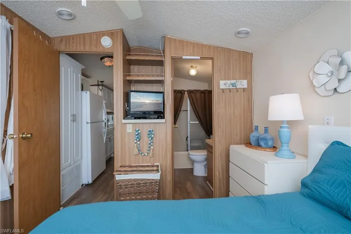 Bedroom with freestanding refrigerator, a textured ceiling, ensuite bathroom, dark wood-style flooring, and wood walls