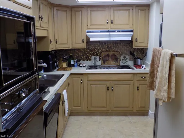 Kitchen featuring under cabinet range hood, white electric cooktop, light countertops, and backsplash