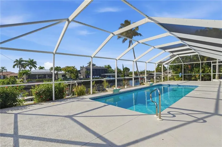 Swimming pool with glass enclosure, a sunroom, a water view, and a patio area
