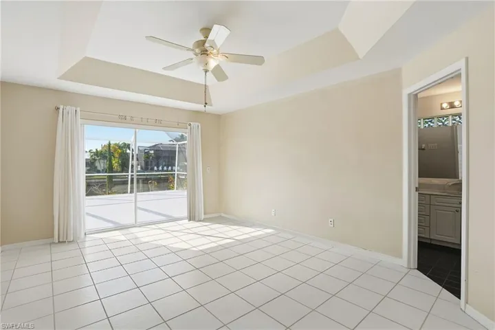 Empty room with a tray ceiling, a ceiling fan, and light tile patterned floors