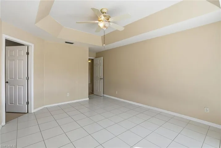 Unfurnished room featuring a raised ceiling, a ceiling fan, and light tile patterned floors