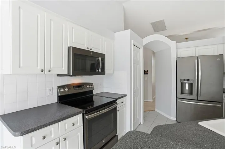 Kitchen with dark countertops, appliances with stainless steel finishes, tasteful backsplash, light tile patterned floors, and white cabinets