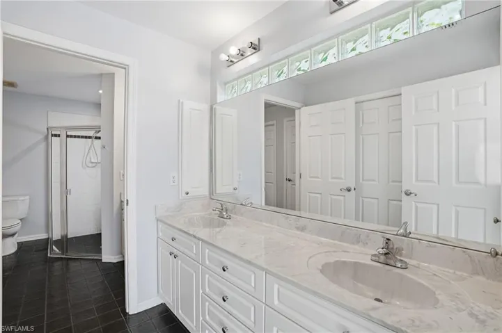 Full bathroom featuring a stall shower, double vanity, and dark tile patterned floors