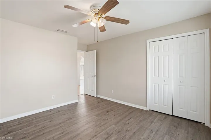 Unfurnished bedroom with wood finished floors, a closet, a ceiling fan, and arched walkways
