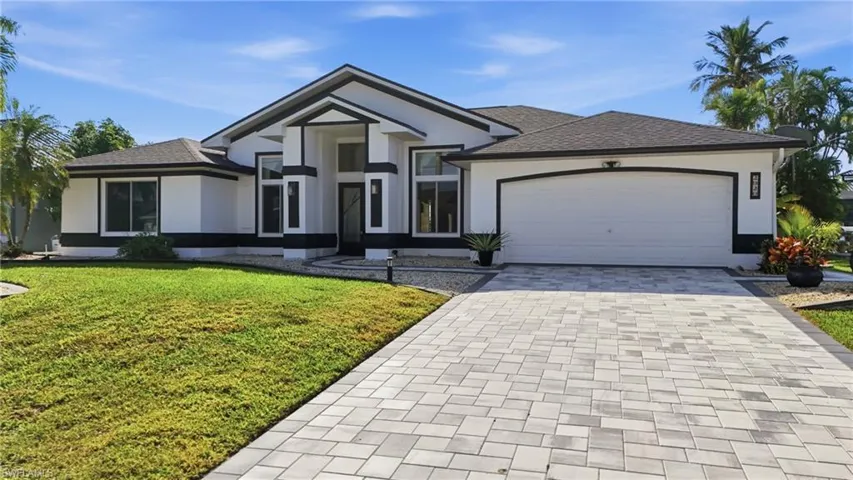 Ranch-style house featuring decorative driveway, a front yard, stucco siding, a shingled roof, and an attached garage