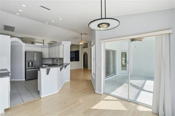 Kitchen with arched walkways, stainless steel fridge, a kitchen breakfast bar, white cabinetry, and recessed lighting