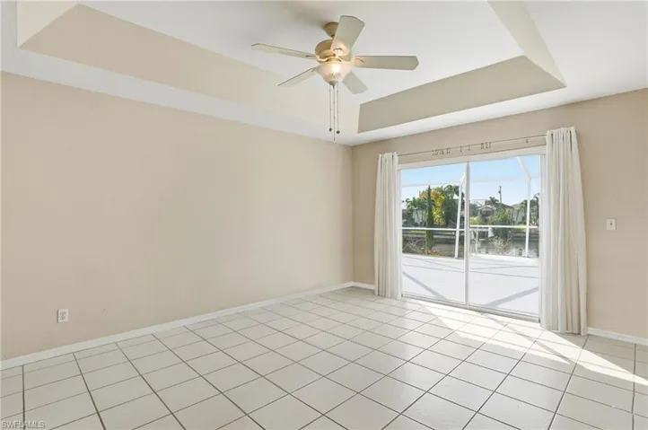 Empty room with a raised ceiling, a ceiling fan, a water view, and light tile patterned flooring